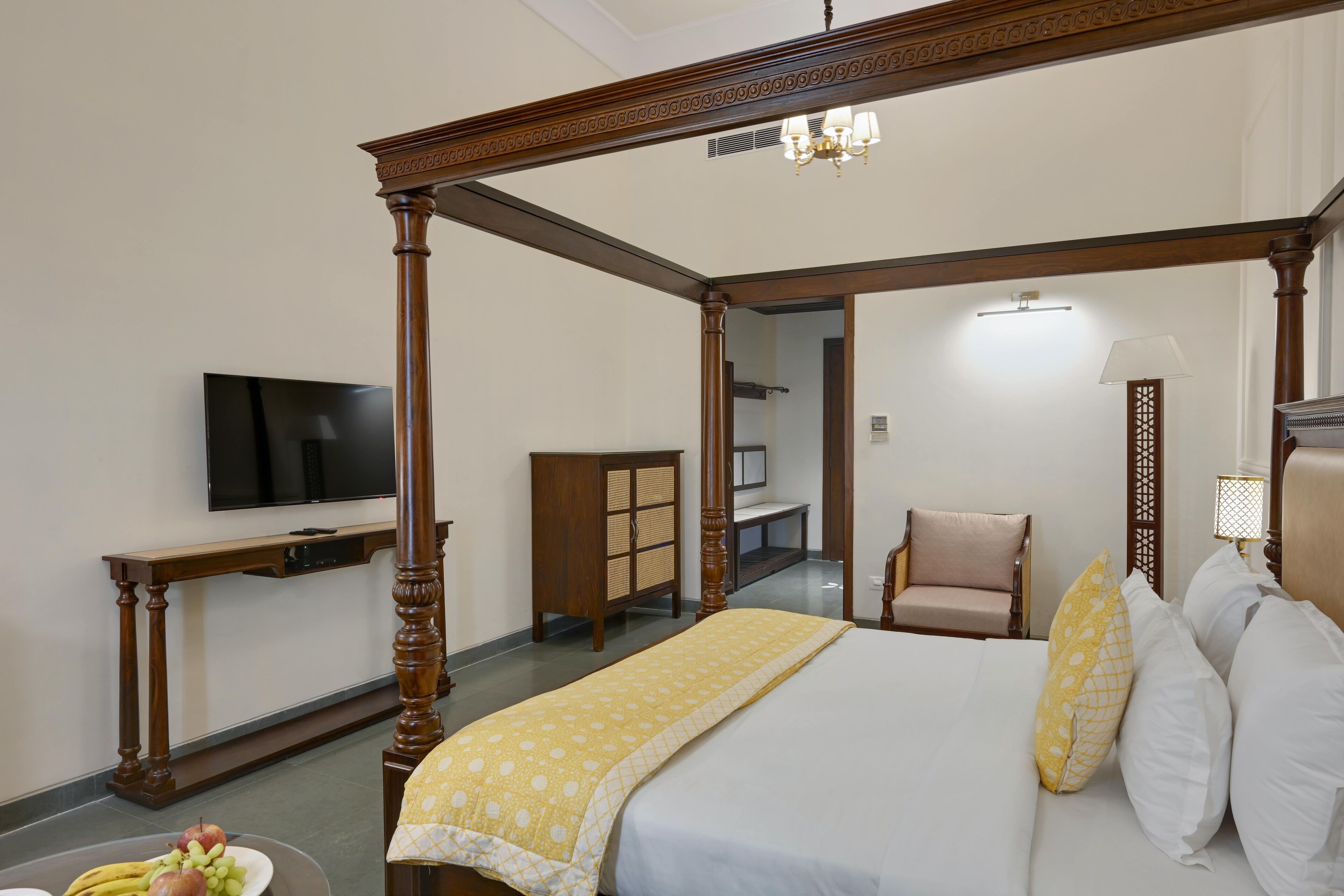 A four-poster bed with a wooden frame, a television on the wall, a desk with a chair, and a lamp.