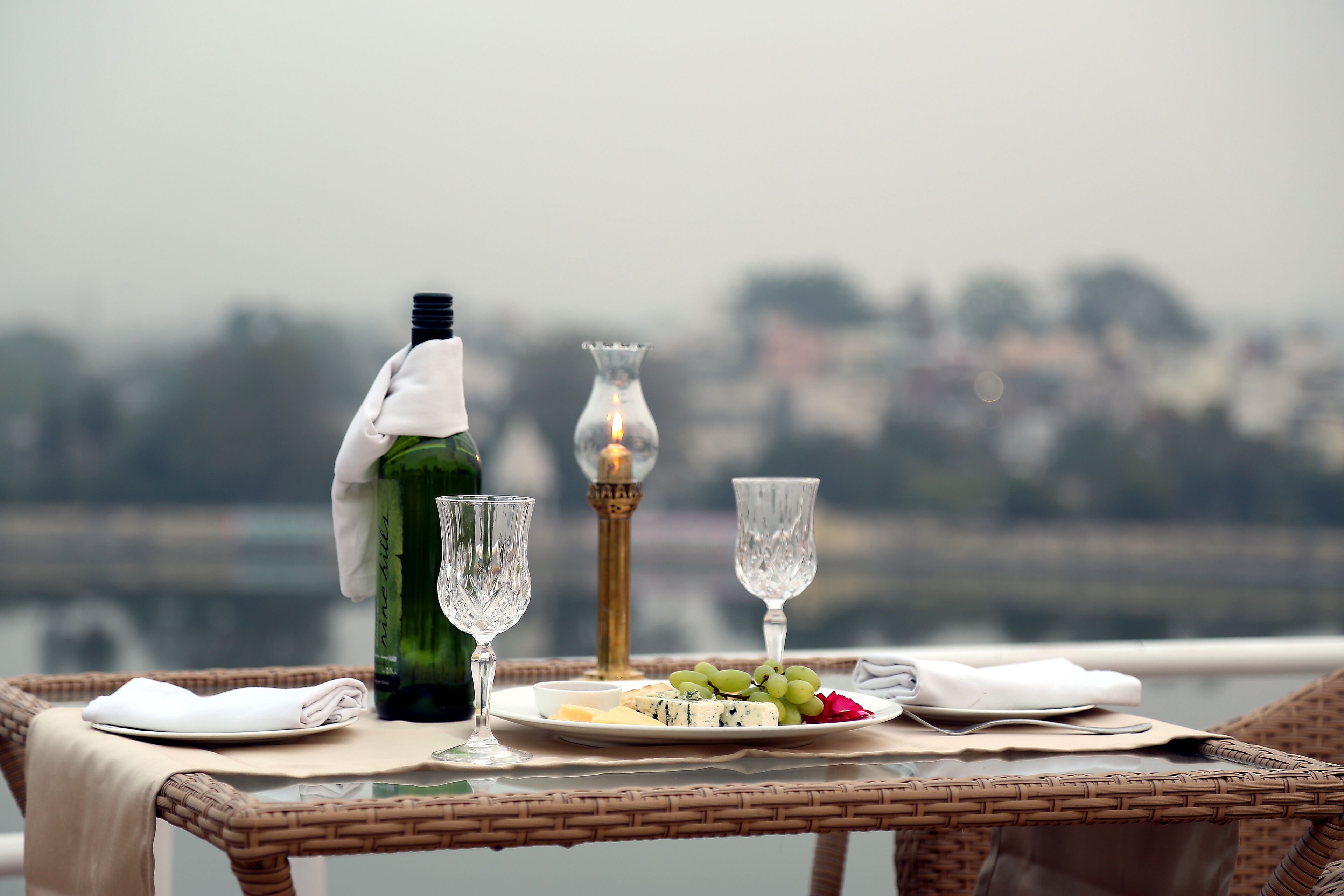 A table with a bottle, glasses, and a plate of cheese and grapes.