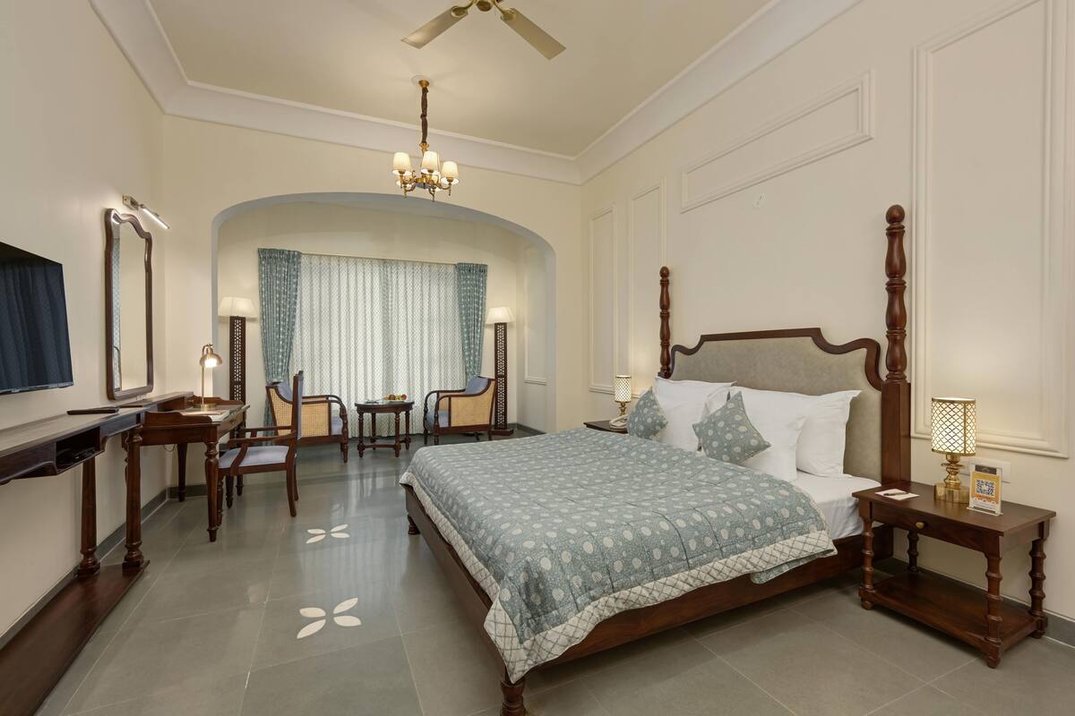 Una habitación de hotel con una cama grande, un escritorio, una silla, un tocador y una araña.
