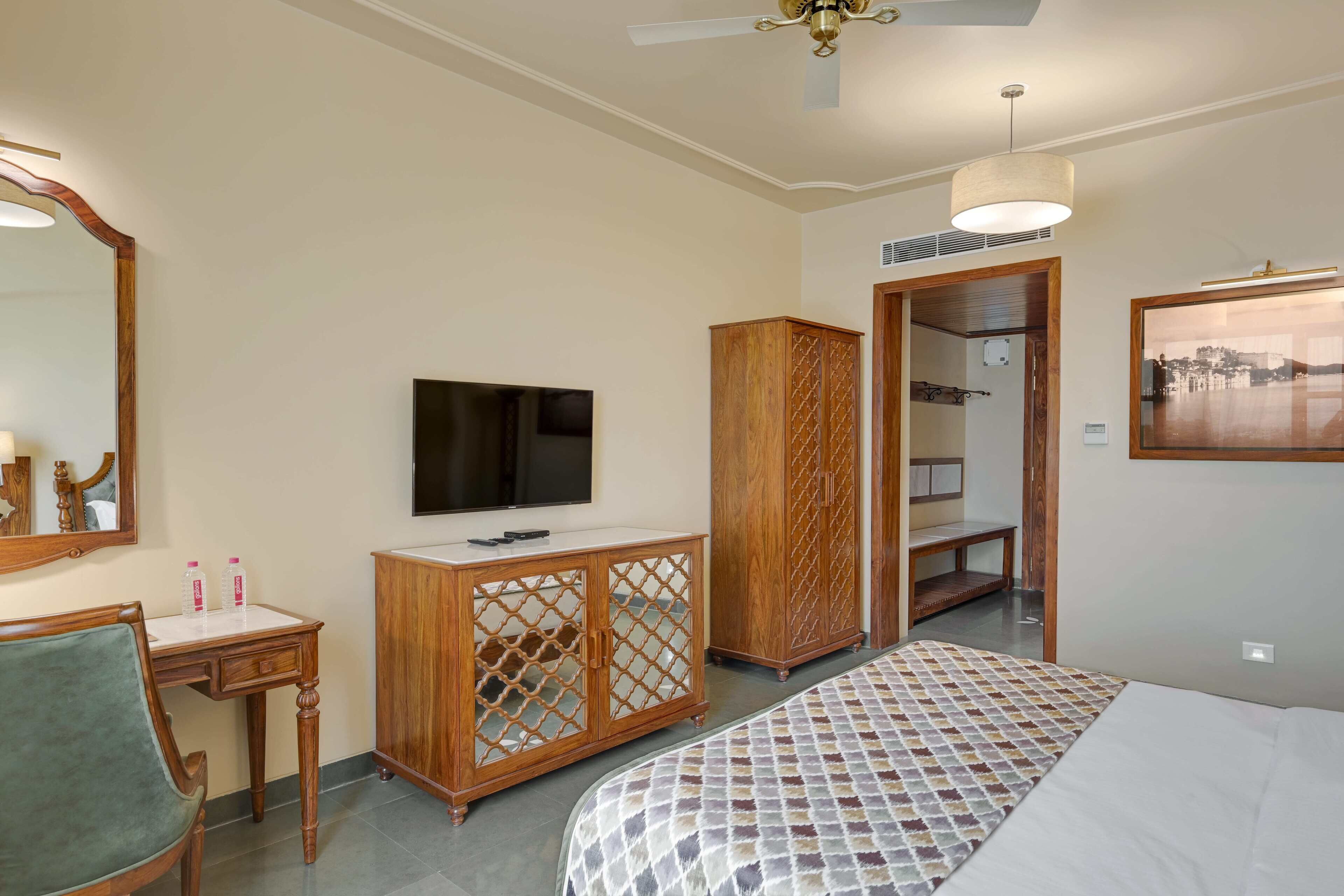 A hotel room with a bed, a TV, a wooden cabinet, a desk, and a wardrobe.