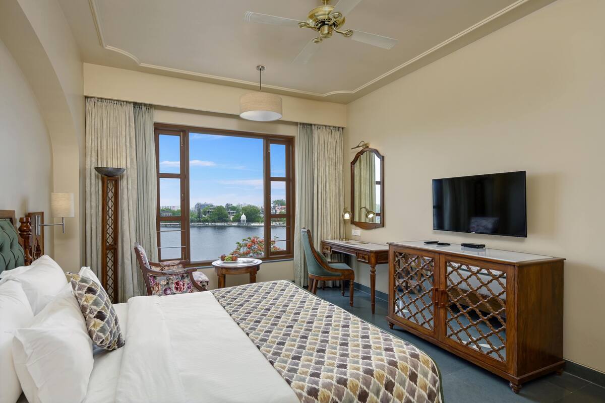 Habitación de hotel con cama, escritorio, televisor y vista a un cuerpo de agua.