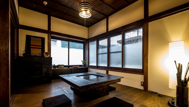 Een traditionele Japanse kamer met tatami vloeren, een lage houten tafel, schuifdeuren en een hangende lamp.