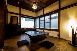 Um quarto japonês tradicional com tatames, uma mesa de madeira baixa, portas deslizantes e um lustre pendente.