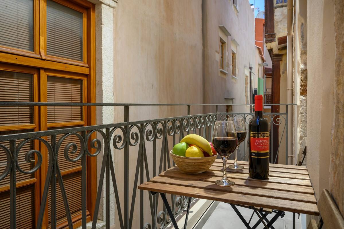 A balcony with a table, a bottle of wine, glasses, and a bowl of fruit.