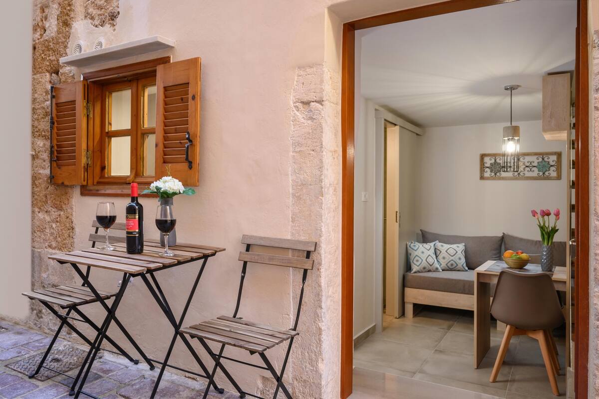 A cozy outdoor seating area with a table and chairs, a bottle of wine, and a vase of flowers.
