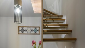 Een moderne woonkamer met een houten trap, een eettafel met een fruitschaal en een vaas met bloemen.