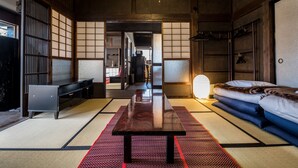 Una habitación japonesa tradicional con suelo de tatami, una mesa de madera baja, una cama con futón y puertas correderas.