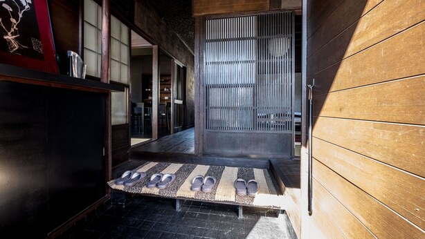 Un interior japonés tradicional con suelo de tatami, una puerta corredera y una pequeña estantería con un cuadro enmarcado.