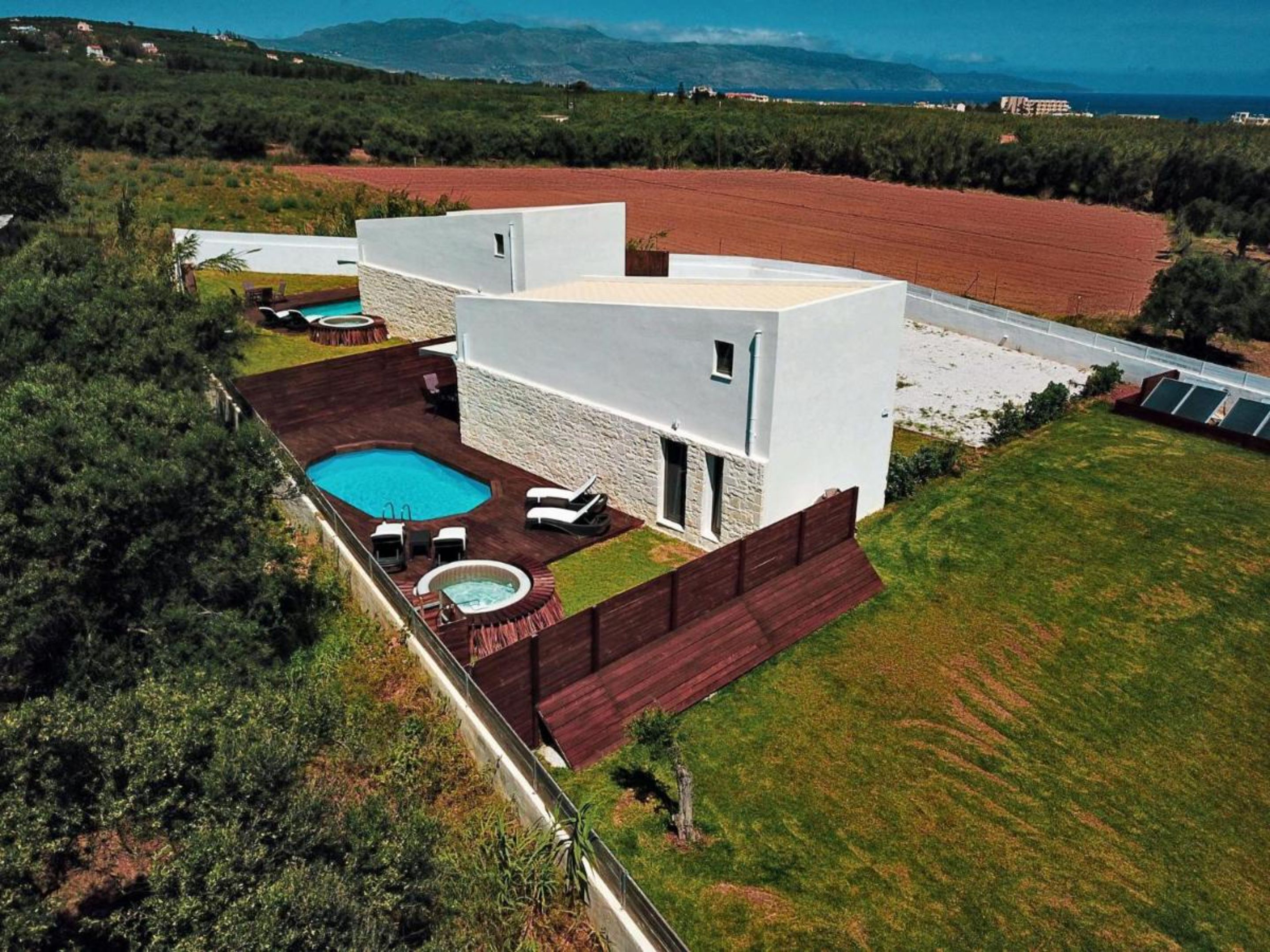 A modern house with a swimming pool, outdoor seating, and a view of the surrounding landscape.