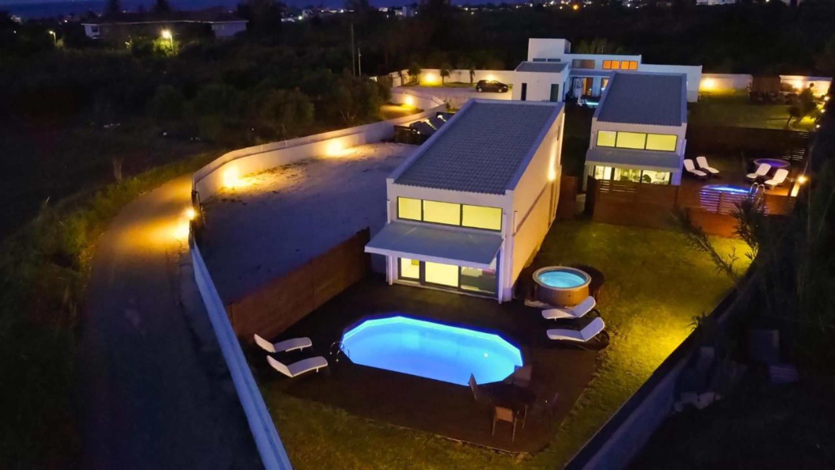Une maison moderne dotée d’une piscine, d’un jacuzzi et d’un patio bien éclairé.