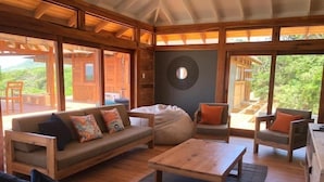 Un salón amplio con suelo de madera, un sofá con cojines de colores, una mesa de centro y un sillón con un cojín naranja.