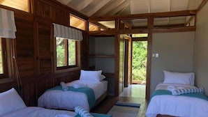 Habitación con tres camas, paredes de madera y ventanas amplias.