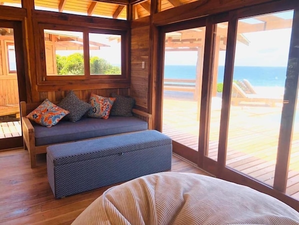 A wooden deck with a cushioned seating area and a view of the ocean.