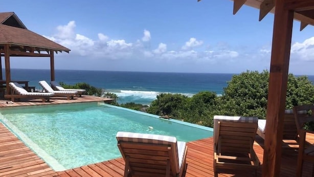 Una terraza de madera con piscina y sillas de descanso con vistas al océano.