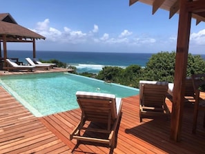 A wooden deck with a pool and lounge chairs overlooking the ocean.