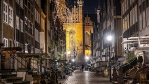 Una calle adoquinada flanqueada por edificios históricos, una torre de iglesia destacada y una escalera que lleva a un nivel superior.