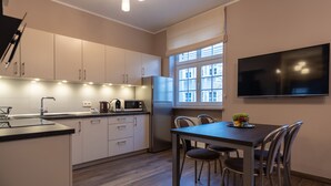 Una cocina moderna con armarios blancos, microondas integrado y refrigerador. Hay una mesa de comedor con sillas y un televisor de pantalla plana montado en la pared.