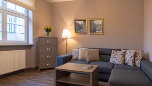 Un salón con un sofá gris, una mesa de centro de madera, una lámpara, un aparador y dos cuadros en la pared.