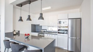Et moderne køkken med en central ø, rustfrie hårde hvidevarer og hængende lamper.