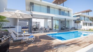 Et moderne hus med swimmingpool, udendørs møbler og grillområde.