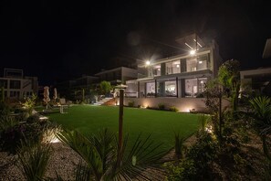 A modern two-story house with a well-lit garden and outdoor seating area.