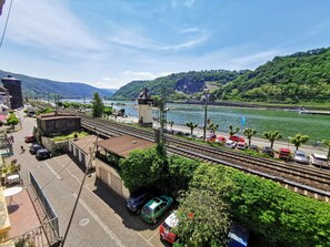 A train station with tracks, a river, and a mountainous backdrop. - Romantisch wohnen in Kaub am Rhein (Kaub)