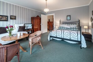 A bedroom with a bed, a sofa, a wicker chair, a small table with a vase of flowers, and a television on a wooden stand. - Romantisch wohnen in Kaub am Rhein (Kaub)