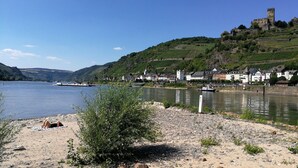 A riverside town with historic buildings, a castle on a hill, and a boat docked near the shore. - Romantisch wohnen in Kaub am Rhein (Kaub)