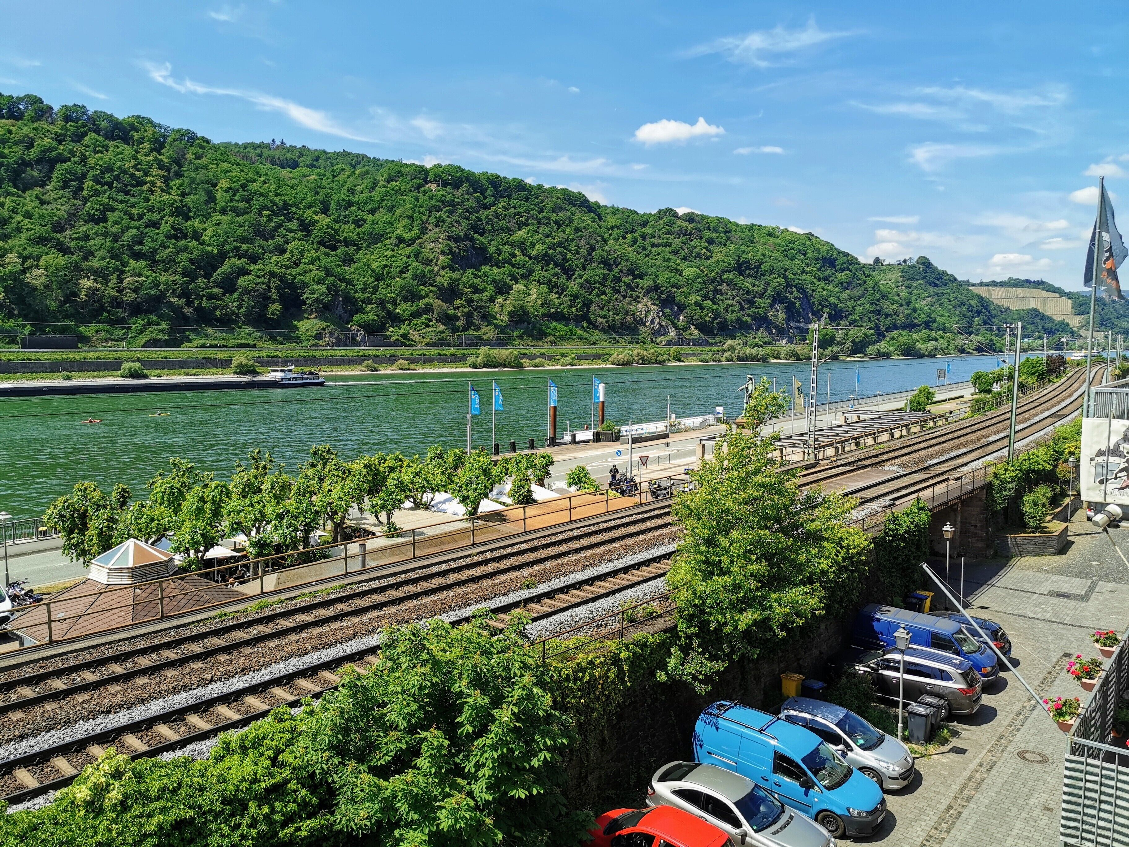 Ein Bahnhof mit mehreren Gleisen, ein Parkplatz mit Autos und ein Fluss im Hintergrund.