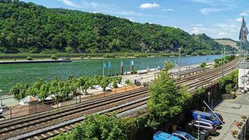 Ein Bahnhof mit mehreren Gleisen, ein Parkplatz mit Autos und ein Fluss im Hintergrund.