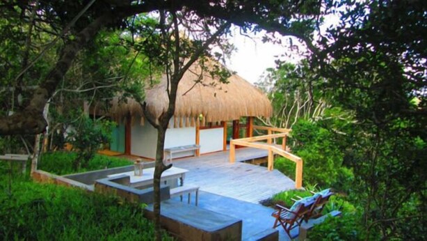 Une structure à toit de chaume dotée d’une terrasse en bois et de chaises longues.