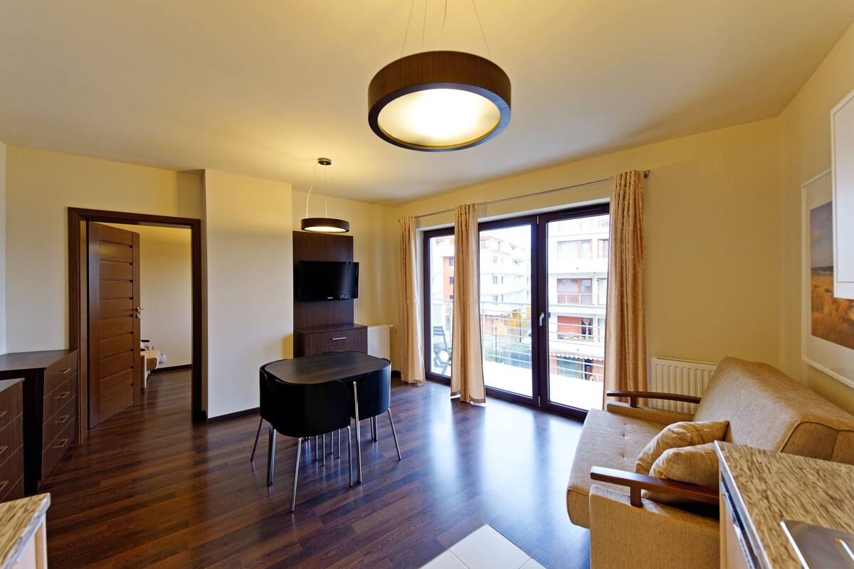 A modern living room with a dining area, a sofa, a TV, and a large window with curtains.
