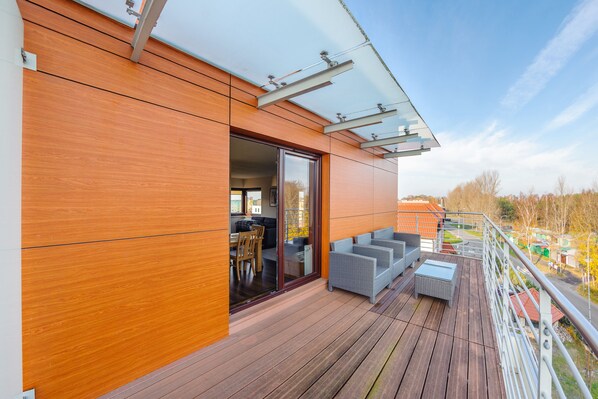 A modern balcony with wooden flooring, a glass door leading to an interior space, and outdoor seating. - Apartamenty Sun & Snow Foka (Hel)