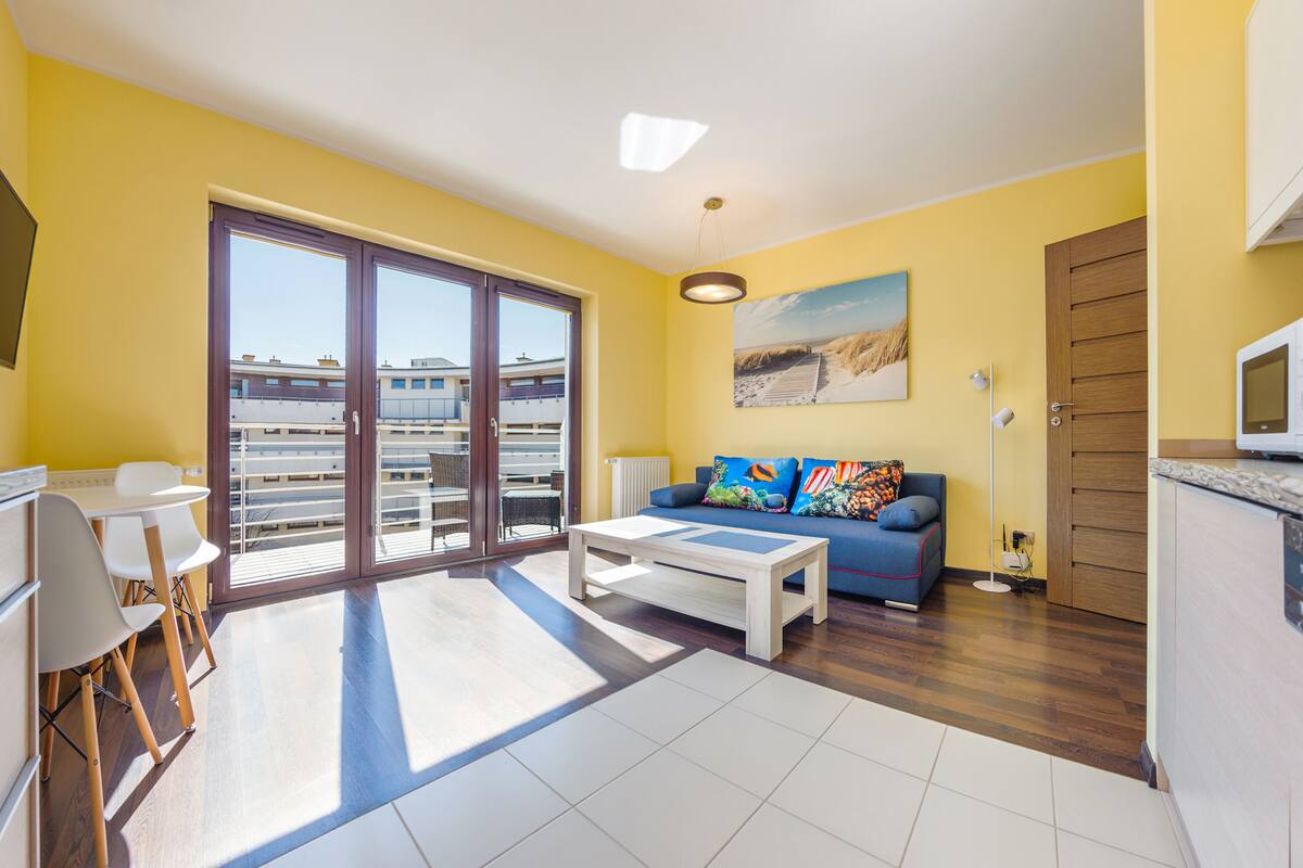A bright living room with a sofa, coffee table, and a dining area with chairs and a table.