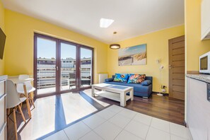 A bright living room with a sofa, coffee table, and a dining area with chairs and a table. - Apartamenty Sun & Snow Foka (Hel)