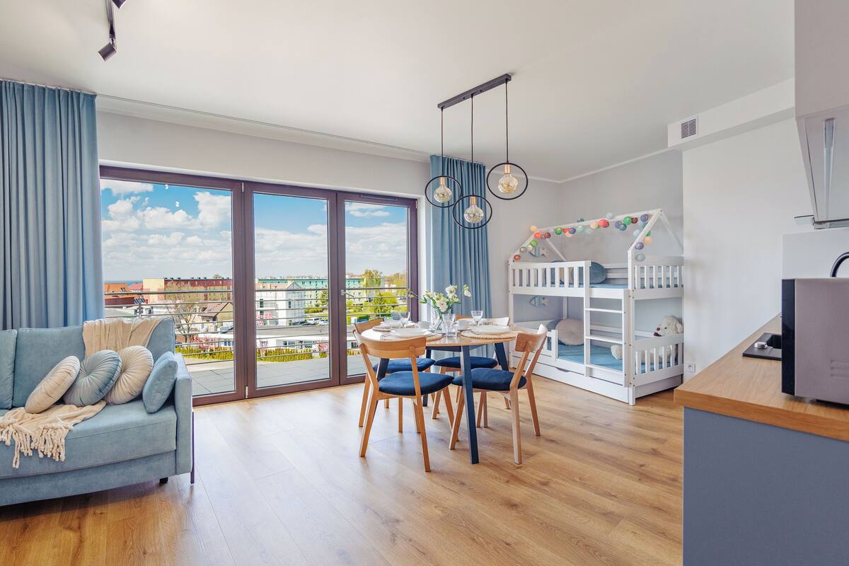 A modern apartment with a balcony, a dining area, a children's play area, and a TV.
