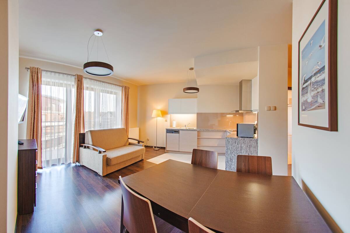 A modern living room with a dining table, sofa, and kitchen in the background.
