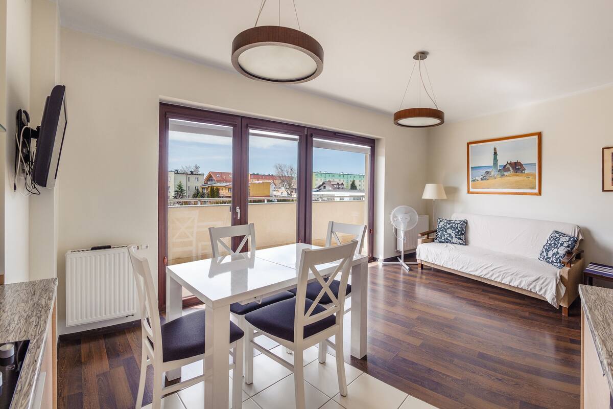 A modern living room with a dining area, large windows, a sofa, and a ceiling fan.