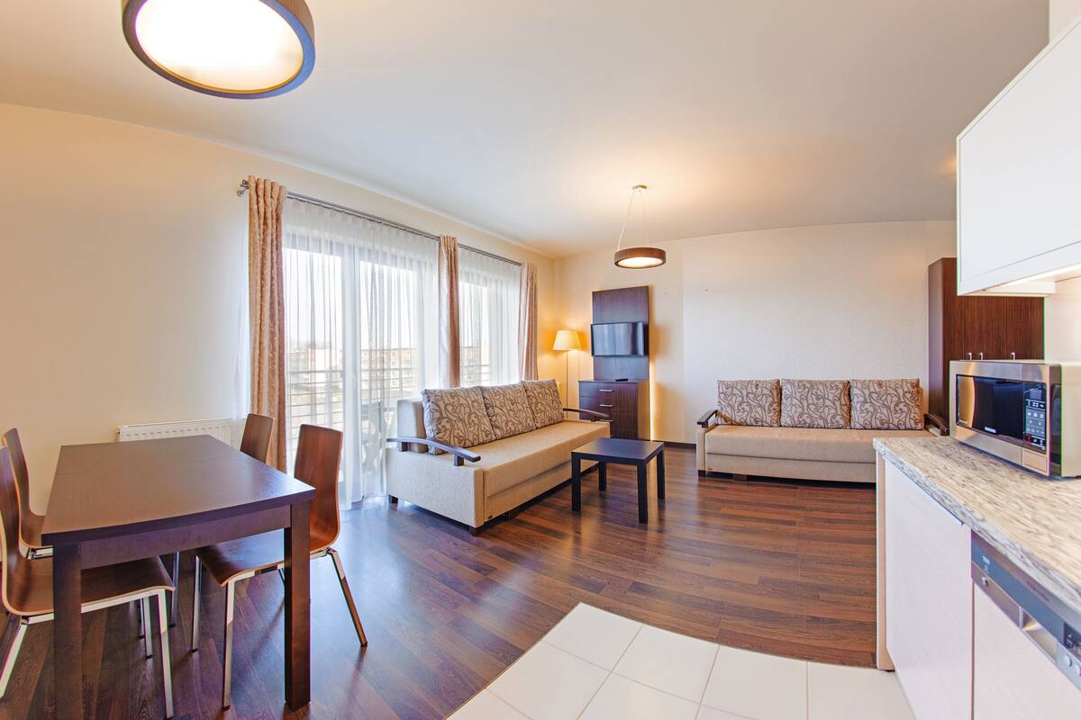 A modern living room with a dining table, sofa, and a kitchen area with a microwave.