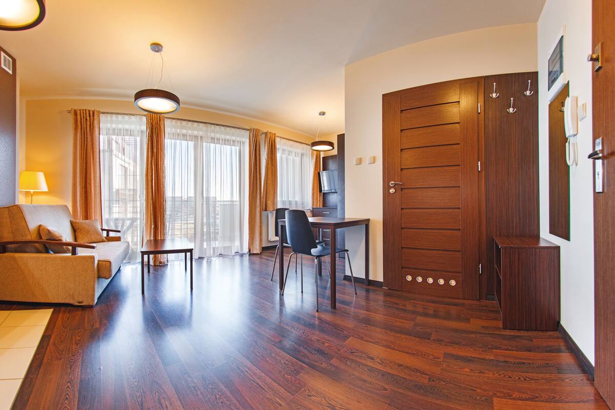A modern hotel room with a wooden floor, a sofa, a dining table, and a desk.