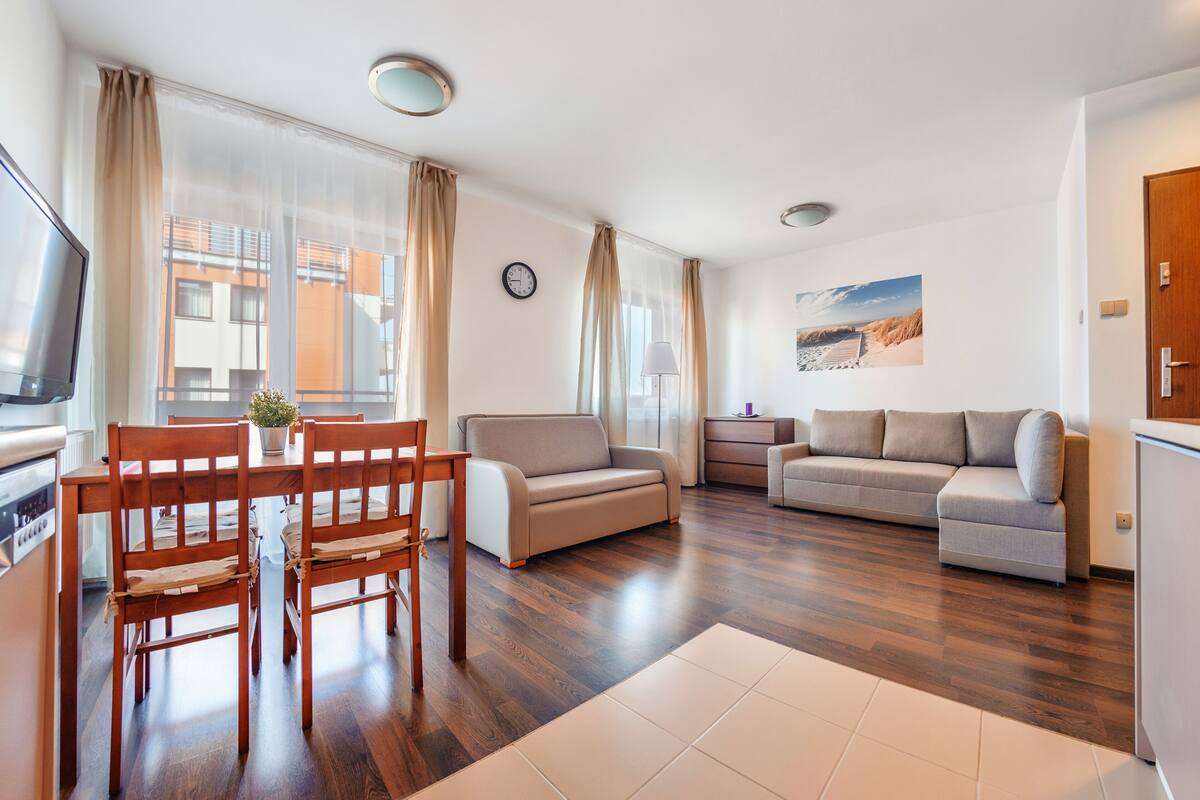 A modern living room with a dining area, two sofas, a TV, and a clock on the wall.