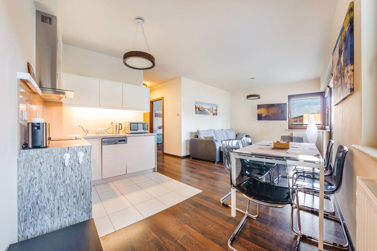 A modern kitchen with white cabinets, a marble countertop, and a dining area with a glass table and black chairs.