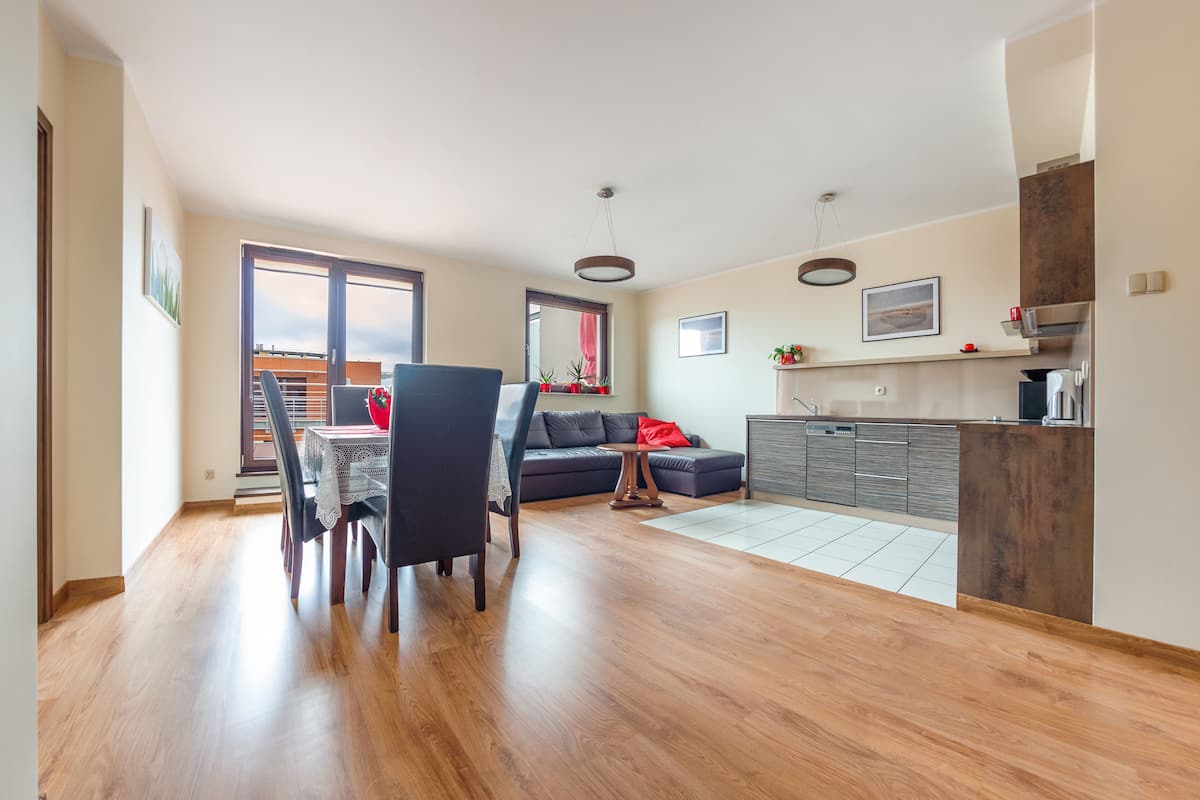 A modern living space with a dining area, sofa, kitchen, and large windows.