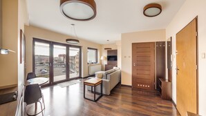 A modern living room with a sofa, a coffee table, and a dining area with chairs. There is a sliding glass door leading to a balcony with a view of the street. - Apartamenty Sun & Snow Foka (Hel)
