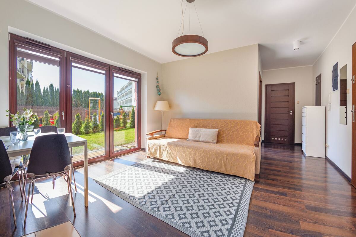 A spacious living area with a sofa, a dining table with chairs, a large window, and a view of a playground.
