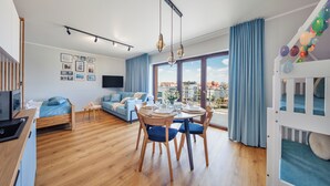 A modern living room with a dining area, a sofa, a TV, and a balcony with a view of the city. - Apartamenty Sun & Snow Foka (Hel)