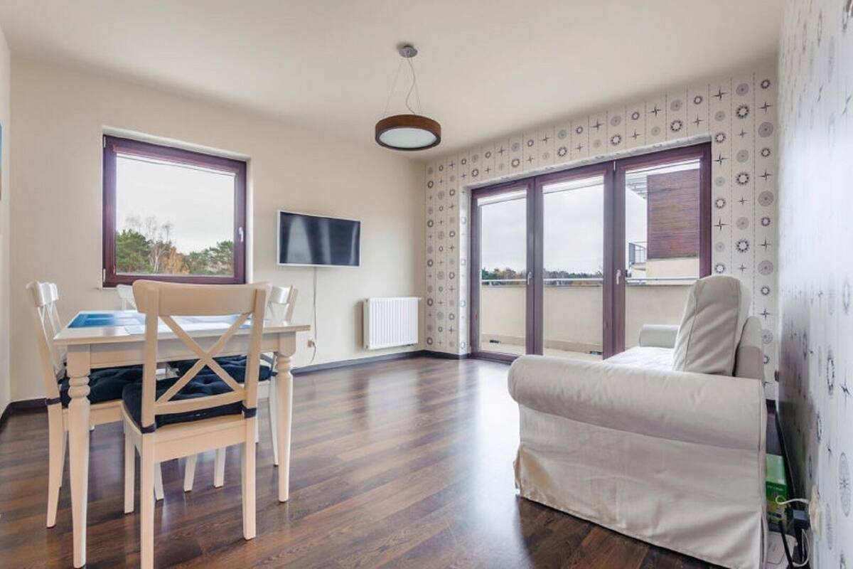 A modern living room with a dining area, large windows, and a flat-screen TV.