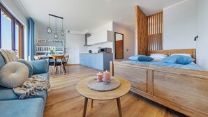 A modern, well-lit room with a wooden bed, a blue sofa, and a dining area with a table and chairs. - Apartamenty Sun & Snow Foka (Hel)