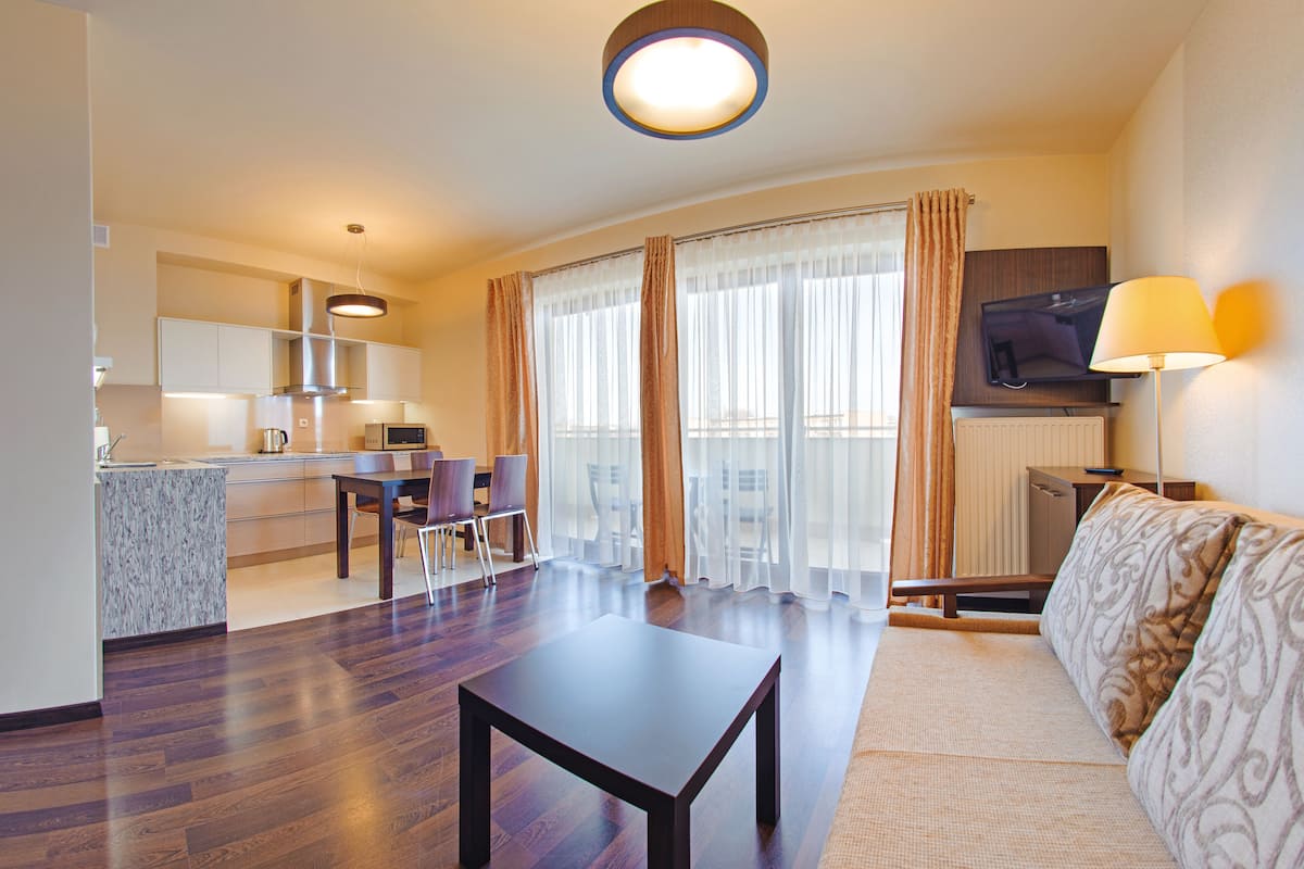A modern hotel room with a dining area, a sofa, a TV, and a lamp.