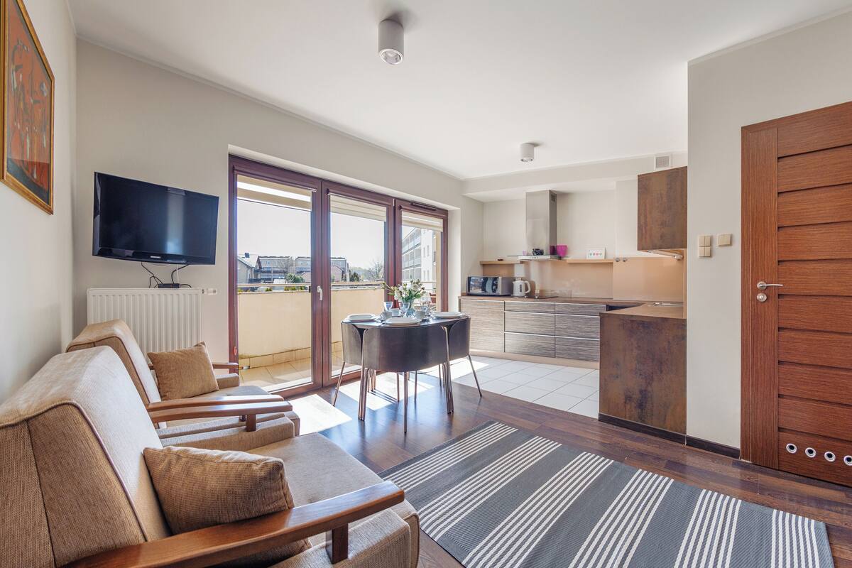 A modern living room with a sofa set, a dining table, and a kitchen area visible through an open door.